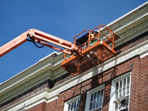 Masonry restoration contractor being lifted to work on the side of a building